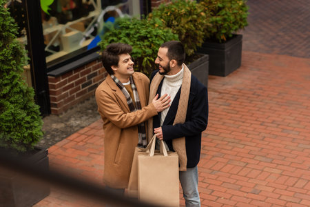 high angle view of gay man laughing near bearded boyfriend with shopping bags on urban streetの写真素材