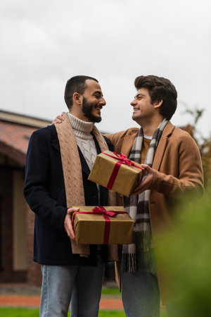 trendy and cheerful gay men with Christmas presents looking at each other on blurred foregroundの写真素材