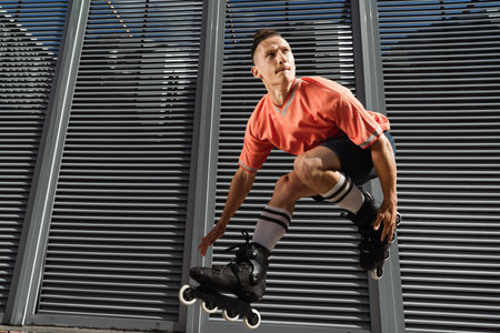 Concentrated man in knee socks and rollers jumping near building on urban street at daytime