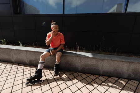 Smiling man in roller blades using earphone and holding paper cup on urban street