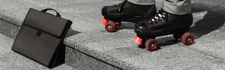 partial view of businessman in roller skates near black briefcase on urban street, banner
