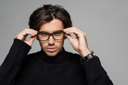 brunette man in black turtleneck wearing eyeglasses isolated on greyの写真素材
