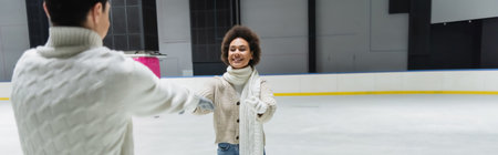Young african american woman outstretching hands to boyfriend on ice rink, bannerの写真素材