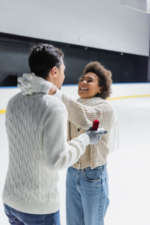 Happy african american woman hugging boyfriend with proposal ring on ice rinkの写真素材