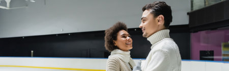 Positive african american woman in scarf looking at boyfriend on ice rink, bannerの写真素材