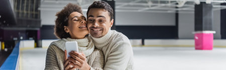 Man hugging african american girlfriend with cellphone on ice rink, bannerの写真素材