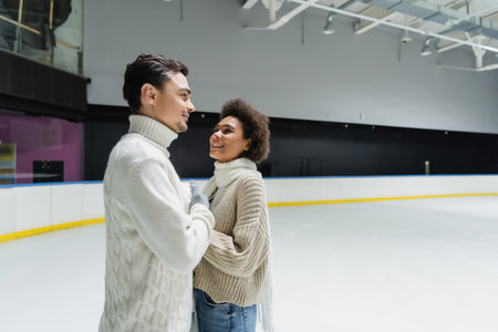 Smiling african american woman looking at boyfriend in sweater on ice rinkの写真素材