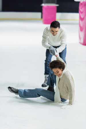 Smiling african american woman sitting on ice near boyfriend on rinkの写真素材