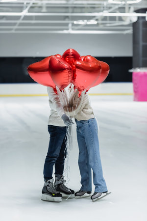 Young couple in warm clothes holding balloons in shape of heart on ice rinkの写真素材