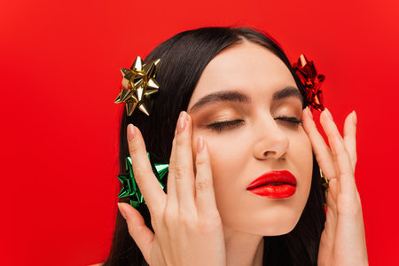 Portrait of young woman with gift bows on hair touching face isolated on redの写真素材