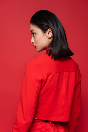 young asian woman in trendy blazer and ear cuff looking away isolated on redの写真素材
