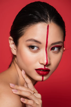 portrait of asian woman with bright artistic visage looking away isolated on redの写真素材
