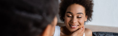 lesbian african american woman touching cheek of happy girlfriend in bedroom, banner