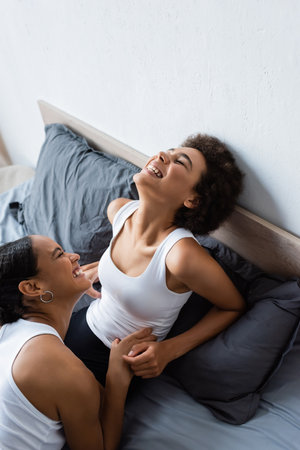 top view of lesbian african american girlfriends laughing while resting on bed