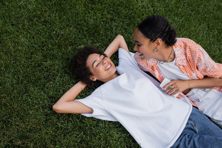 top view of joyful african american lesbian woman holding smartphone and looking at girlfriend lying...