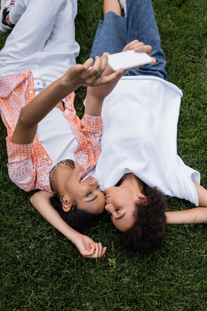 top view of happy african american lesbian woman holding smartphone and taking selfie with...