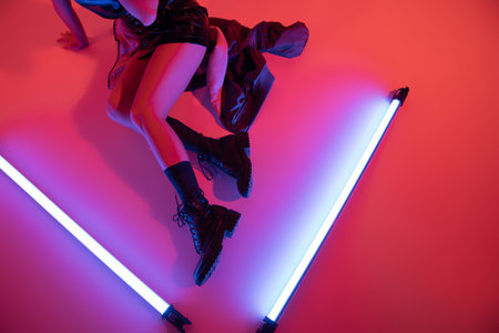 top view of cropped woman in black leather boots near purple neon lamps on carmine red backgroundの写真素材