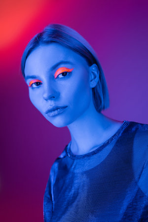 young woman with glowing makeup in blue neon light on purple and coral background