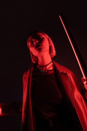low angle view of woman holding neon lamp with red light on black background