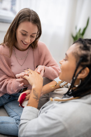 lesbian woman making proposal and wearing engagement ring on finger of blurred african american girlfriendの写真素材
