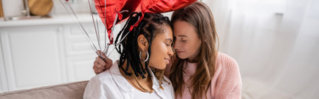 sensual lesbian woman holding red balloons near african american girlfriend on valentines day, bannerの写真素材