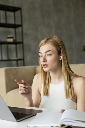 Blonde coach in earphone pointing with finger during video call on laptop at home