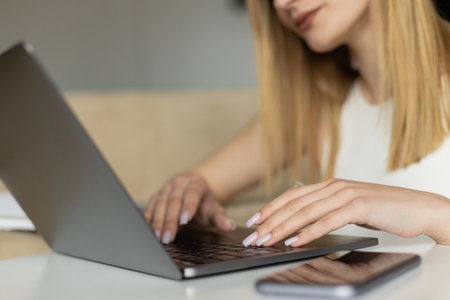 Cropped view of blurred coach using laptop near mobile phone with blank screen at homeの写真素材