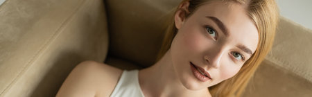 Top view of young woman looking at camera while lying on couch, banner