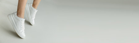 cropped view of woman in white laced sneakers standing on tiptoes on grey background with copy...