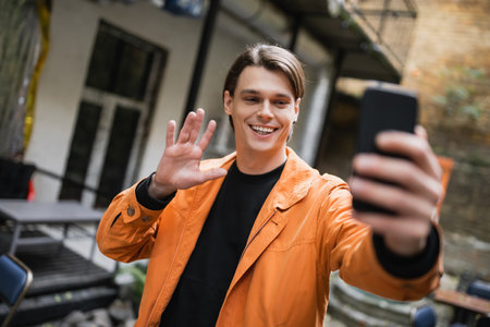 Smiling man having video call on smartphone on terrace of cafeの写真素材