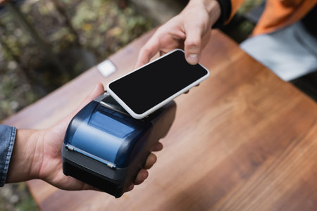 Cropped view of man paying with smartphone near waitress with payment terminal in cafe