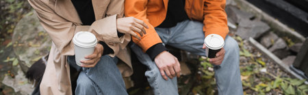 Cropped view of stylish couple holding paper cups in outdoor cafe, banner
