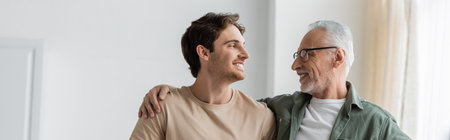 young and happy man looking at senior father embracing his shoulders, banner