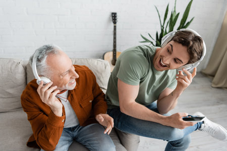 high angle view of excited father and son looking at each other while listening music in wireless...