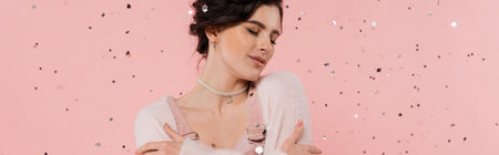 pretty brunette woman in cozy cardigan standing with closed eyes near confetti on pink background, bannerの写真素材