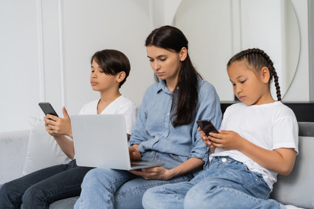 Asian children using cellphones while mother working on laptop at homeの写真素材