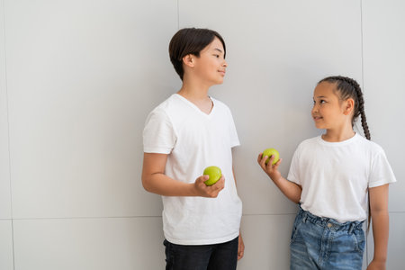 Smiling asian children holding apples near wall at homeの写真素材