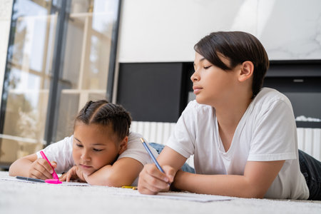 Asian kids drawing on papers while lying on floor at home