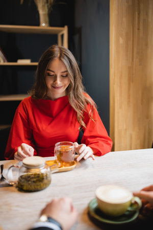 cheerful young woman in red dress looking at glass cup with green tea near boyfriendの写真素材