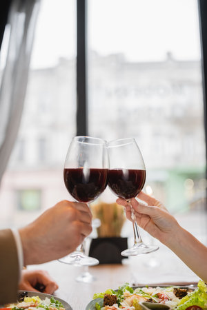 partial view of couple clinking glasses with red wine during celebration on valentines dayの写真素材