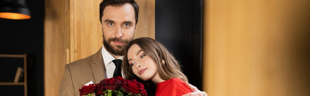 young woman looking at red roses and leaning on boyfriend on valentines day, bannerの写真素材