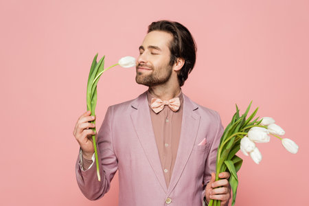 Brunette host of event in jacket smelling tulip isolated on pinkの写真素材
