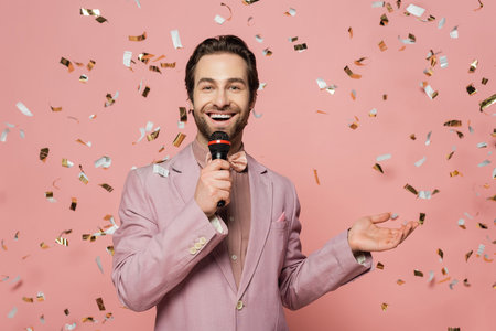 Positive host of event holding microphone under falling confetti on pink backgroundの写真素材