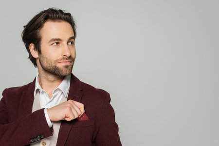bearded showman adjusting handkerchief in pocket of blazer isolated on greyの写真素材
