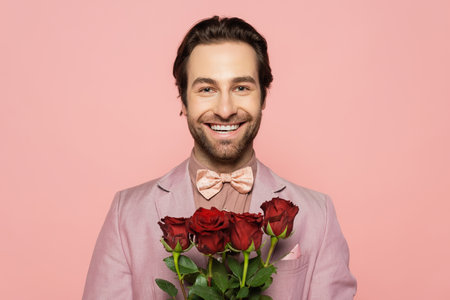 Portrait of positive host of event holding roses and looking at camera isolated on pinkの写真素材