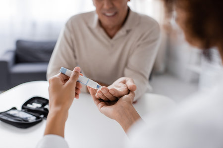 partial view of african american doctor taking blood sample of blurred mature patient with lancet penの写真素材