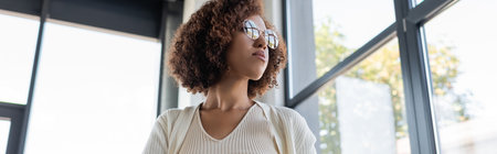 Low angle view of african american businesswoman in eyeglasses looking away in office, banner