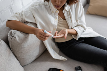 Cropped view of african american woman with diabetes using lancet pen on couch at home