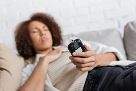 African american woman with diabetes feeling unwell and holding glucometer at homeの写真素材