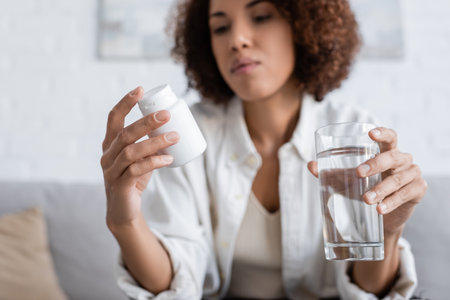Blurred african american woman with diabetes holding pills and water at homeの写真素材